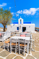 Taverna tables on square with typical white Greek church in Naoussa port, Paros island, Cyclades, Greece