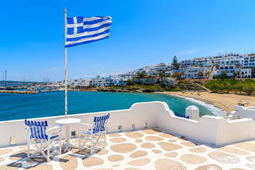 Chairs with table on a terrace with Greek flag in Naoussa village, Paros island, Greece
