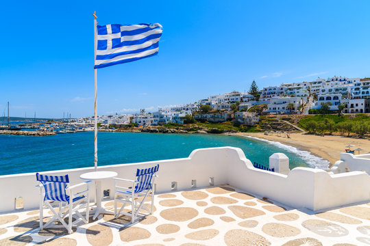 Chairs with table on a terrace with Greek flag in Naoussa village, Paros island, Greece