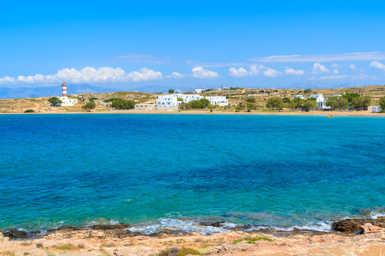 Blue sea bay with lighthouse and holiday apartments in distance in Naoussa town, Paros island, Greece