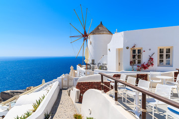 Typical white windmill on street of Oia village with blue sea in background, Santorini island, Greece