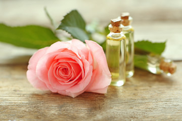 Bottles of aroma oil with roses on wooden table