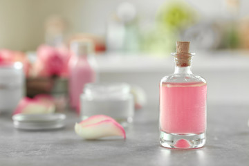 Bottle of aroma oil with flower petal on light background