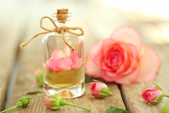 Bottle of aroma oil with roses on wooden table