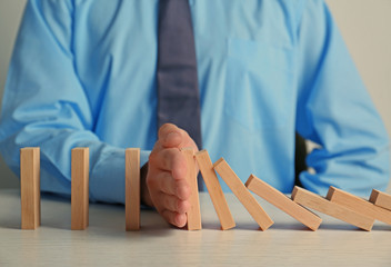 Businessman hand trying to stop toppling dominoes on table