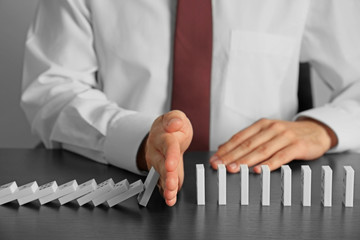 Businessman hand trying to stop toppling dominoes on table