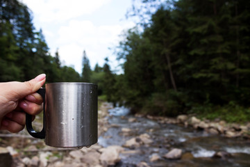 Metal travel mug stands on a log on the background of a mountain