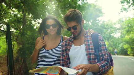 Adorable young smiling couple holding a map on the hands, walking on a green park.