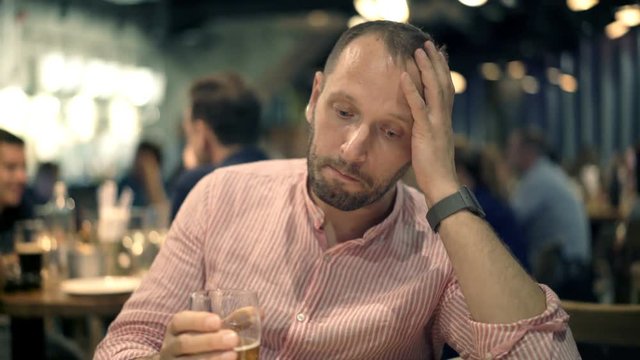 Lonely, unhappy man drinking beer sitting in cafe at night
