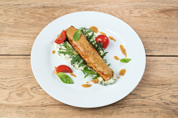 Grilled salmon steak with mashed potatoes, herbs and fresh tomatoes served on a white plate on old wooden table