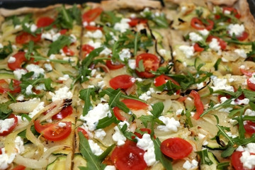 Vegetarian pizza in a pan, with mozzarella, onion, garlic, zucchini, cherry tomato, cottage cheese and salad rocket. Top view.