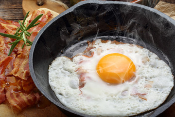 Fried hot egg with hot bacon pieces in a cast iron skillet