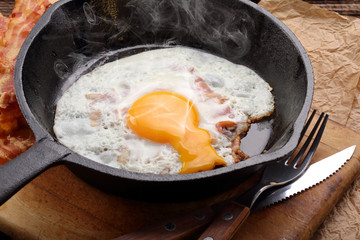 Fried hot egg with hot bacon pieces in a cast iron skillet