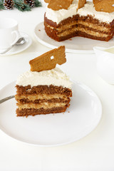 A slice of Gingerbread cake (Spekulatius Torte) with Spekulatius cookie as decoration on top, traditionally eaten in winter. The cut cake and Christmas decoration in the background.