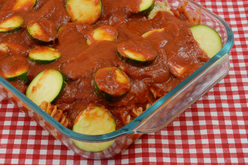 Casserole layer preparation of whole wheat pasta, thin chicken breast and sliced zucchini and tomato sauce