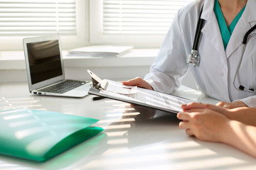 Fototapeta premium Doctor pointing into medical history form and discussing something with her patient. Close-up.