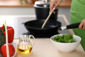 Fresh vegetables, salad and vegetable oil at the background of  woman is cooking by the stove in the kitchen