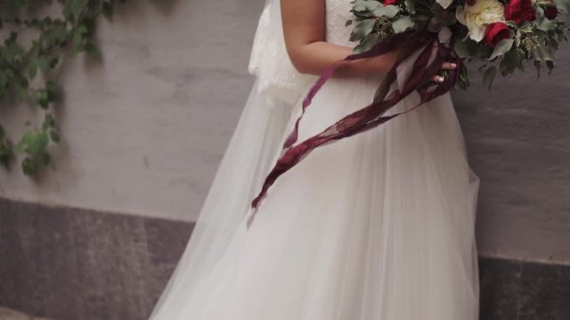Young caucasian woman in white wedding dress holds a beautiful bouquet of red and white in her hands