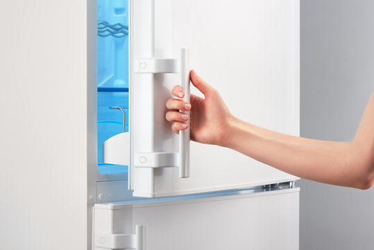 Female hand opening white refrigerator door on gray