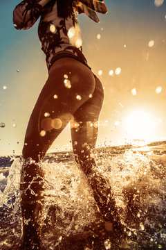 Beach girl stand in splashes in water. Model hold small fins in