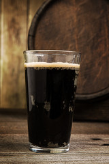 Russian Imperial Stout in pint glass on wood background and barr