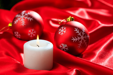 Christmas balls and candle on red satin background