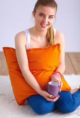 Smiling young woman sitting on a white floor with pillow © lenets_tan