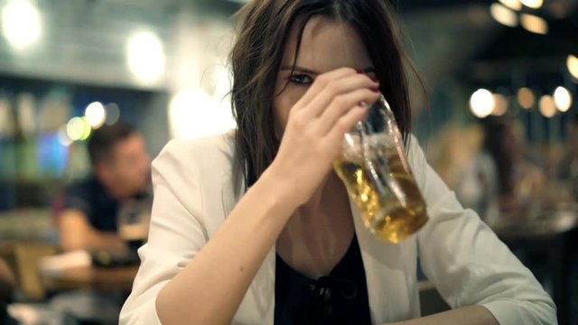 Drunk woman drinking beer in cafe at night
