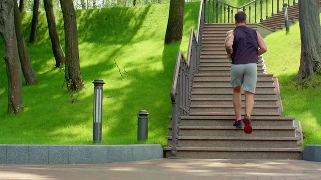 Fitness man run up stairs in slow motion. Young man running upstairs with dumbbells at park. Fit man in sport clothes run up stairs. Man fitness workout. Healthy lifestyle. Man climbing stairs