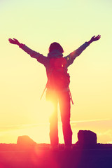 Happy hiker freedom having reached summit goal with success at sunset. Silhouette of woman with backpack celebrating winning standing at mountain top with arms up in celebration during hiking travel.