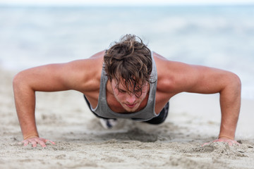 Fit fitness man exercising arms muscles doing exercise push ups exercises. Caucasian male fitness athlete model cross-training push-up on beach outdoor. Pushups trainer working out in summer on beach.
