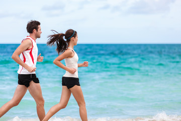 Fitness interracial couple runners running on beach. Running couple jogging together outside on ocean background. Athletes training cardio outdoors working out. Fit Asian woman, Caucasian man.