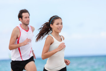 Fitness interracial couple runners running on beach. Running couple jogging together outside on ocean background. Athletes training cardio outdoors working out.
