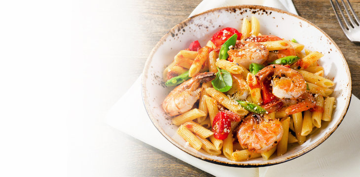 Penne pasta with shrimp, tomatoes and herbs on wooden background