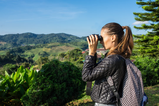 The tourist on the tea field looks in the field-glass at mountains. To look in a distance. The girl with the field-glass dressed vdinsovy trousers, a shirt and a backpack