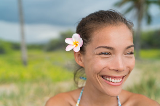 Fototapeta Hawaii Asian girl wearing plumeria flower hair accessory. Fresh real natural pink plumeria flower, a polynesia typical decoration. Happy smiling woman wearing a hawaiian typical flower in her hair.