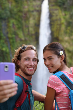 Hawaii couple tourists taking travel phone selfie self portrait with camera phone on Hawaii, Big Islands, Akaka Falls. Happy cheerful young multicultural couple on travel.