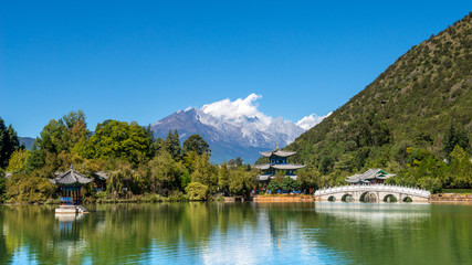 Fototapeta na wymiar Black Dragon Pool to the Five Phoenix Tower and the Five Holes Bridge. In the background is Yulong Xue Shan (Jade Dragon Snow Mountain). The Old Town of Lijiang, Yunnan, China.