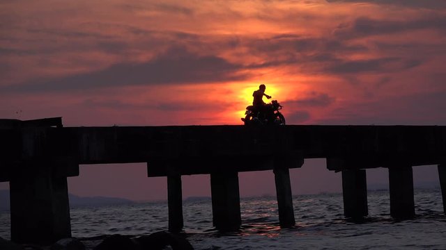 Silhouette of a man of on a motorcycle taking selfies with a glorious sunset in background. Filmed in 4k video in Thailand.