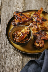 Grilled chicken wings with chutney on a plate with the effect of craquelure on rough wooden background. Selective focus. Toned image 