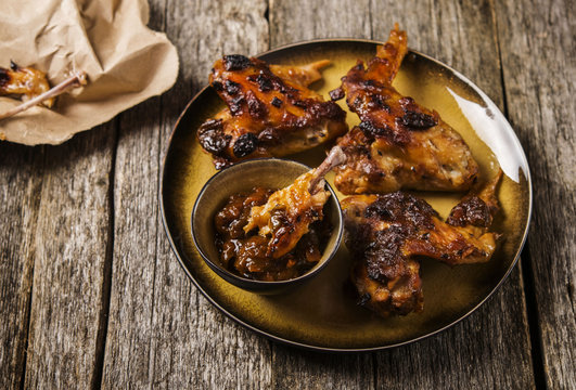 Grilled chicken wings with chutney on a plate with the effect of craquelure on rough wooden background. Selective focus 