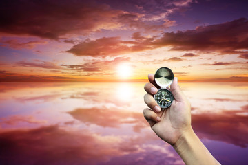 Hand holding compass on sunset