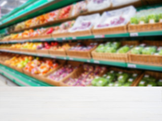 Wooden empty table in front of blurred supermarket vegetables shelf