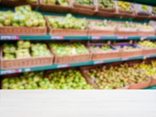 Wooden empty table in front of blurred supermarket vegetables shelf