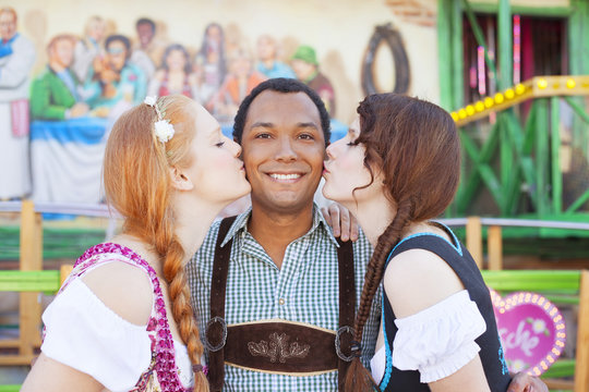 Young man getting kissed on the cheek by two german girls at Oktoberfest