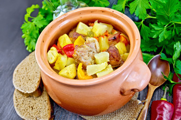 Roast meat and vegetables in clay pot on board
