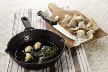 roasted garlic in a cast iron pan and fresh garlic on a wooden b