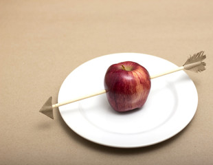 Apple pierced by toy arrow handmade on white dish.