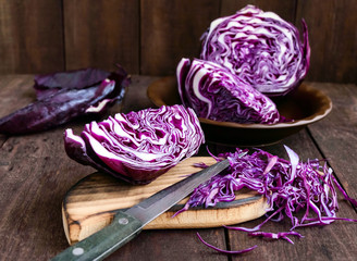 Red cabbage cutting into pieces with a knife on a dark wooden background. Ingredient for cooking vegetable dishes.