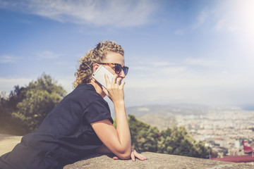 Side view of a young woman dressed in a black T-shirt and sunglasses, standing and talking on the phone. In the background landscape with aerial view, clouds in the sky. Girl uses the gadget.